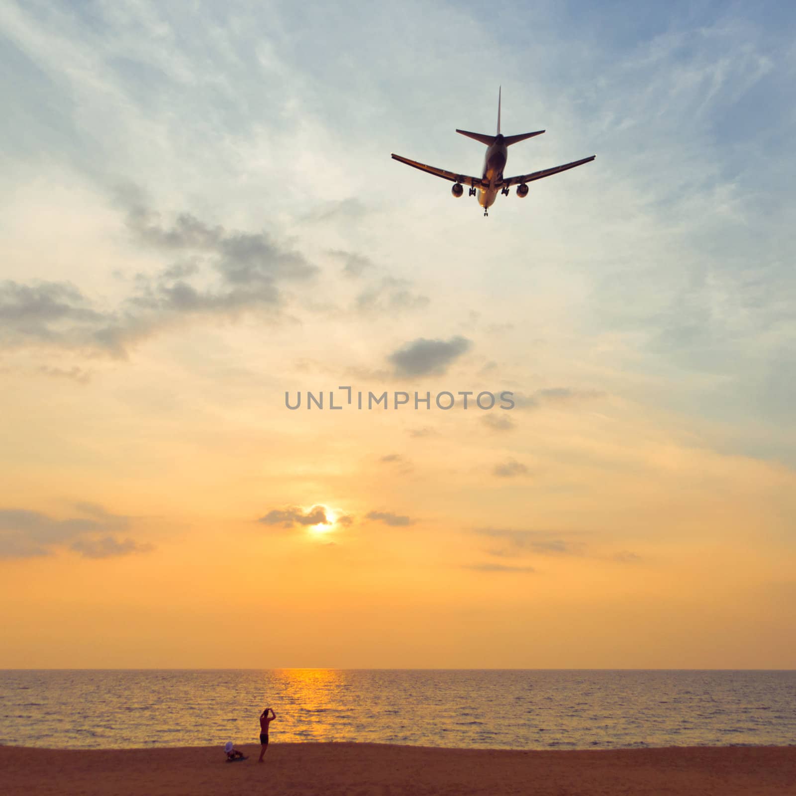 Man on the beach is looking on the airplane flying to the horizon