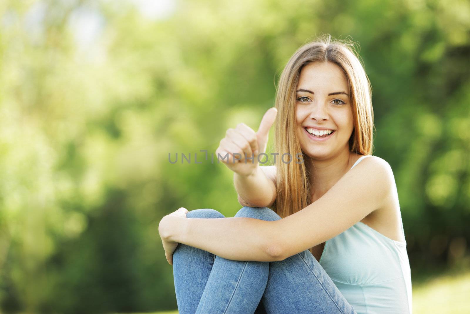 Young smiling blond female outdoors showing thumb up sign