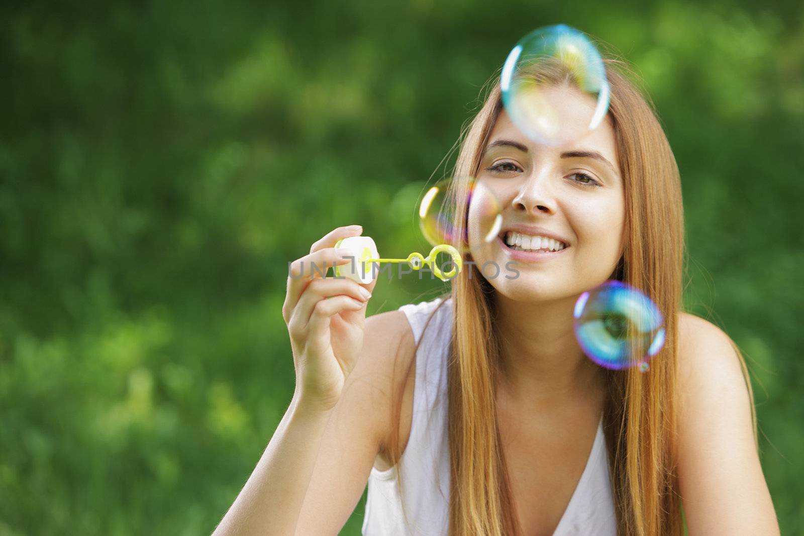 Beautiful young woman smiling and blowing bubbles outdoor in the nature.