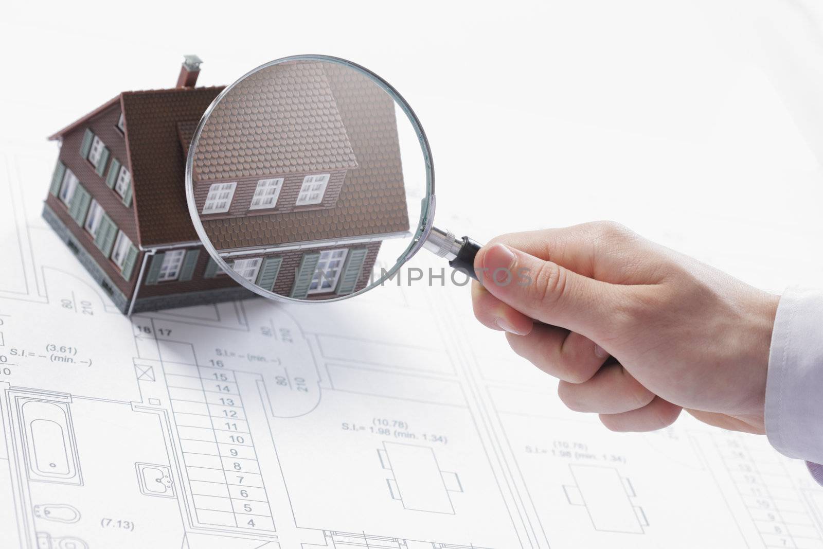 Concept image of a home inspection. A male hand holds a magnifying glass over a miniature house. 