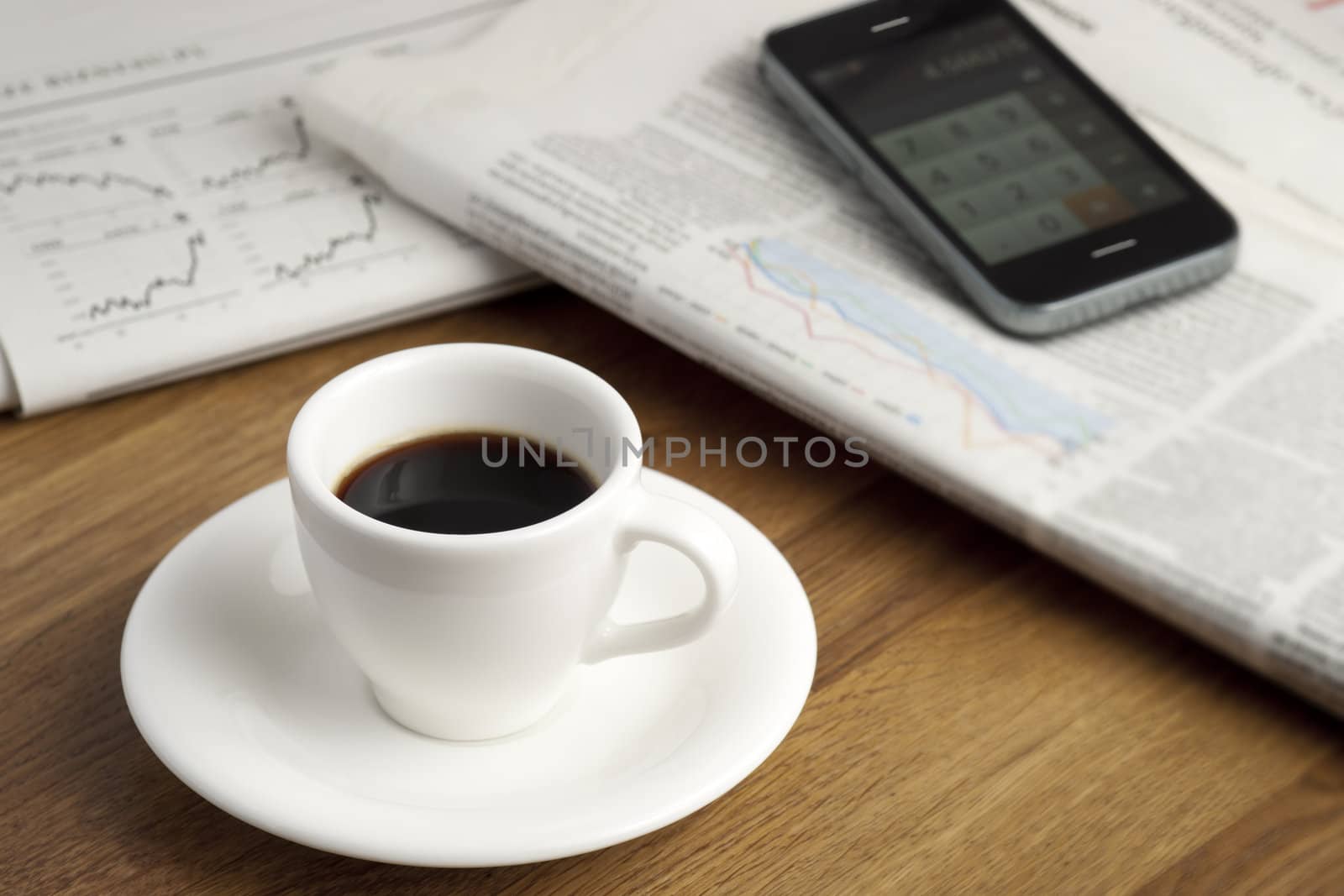 Coffee cup, smartphone and business newspapers with charts.