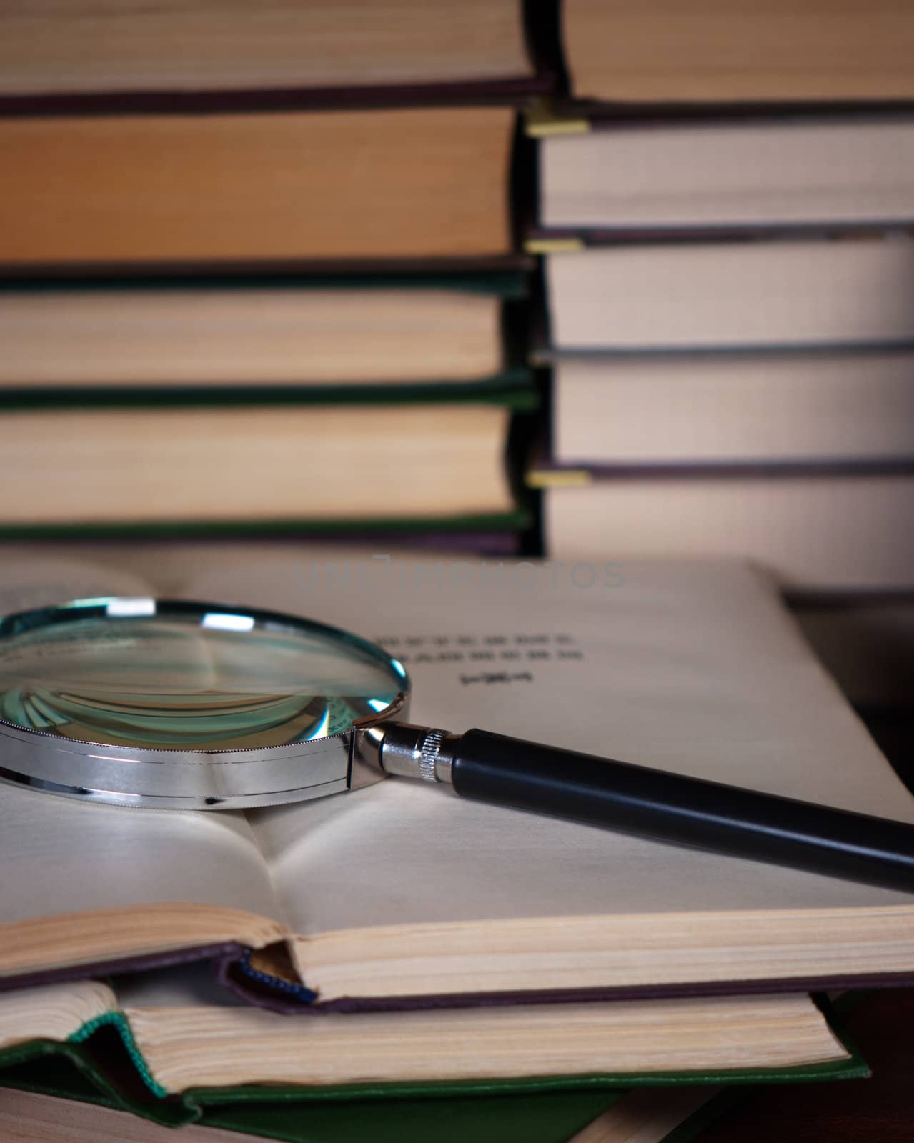 Magnifying glass on a pile of open books. by BPhoto