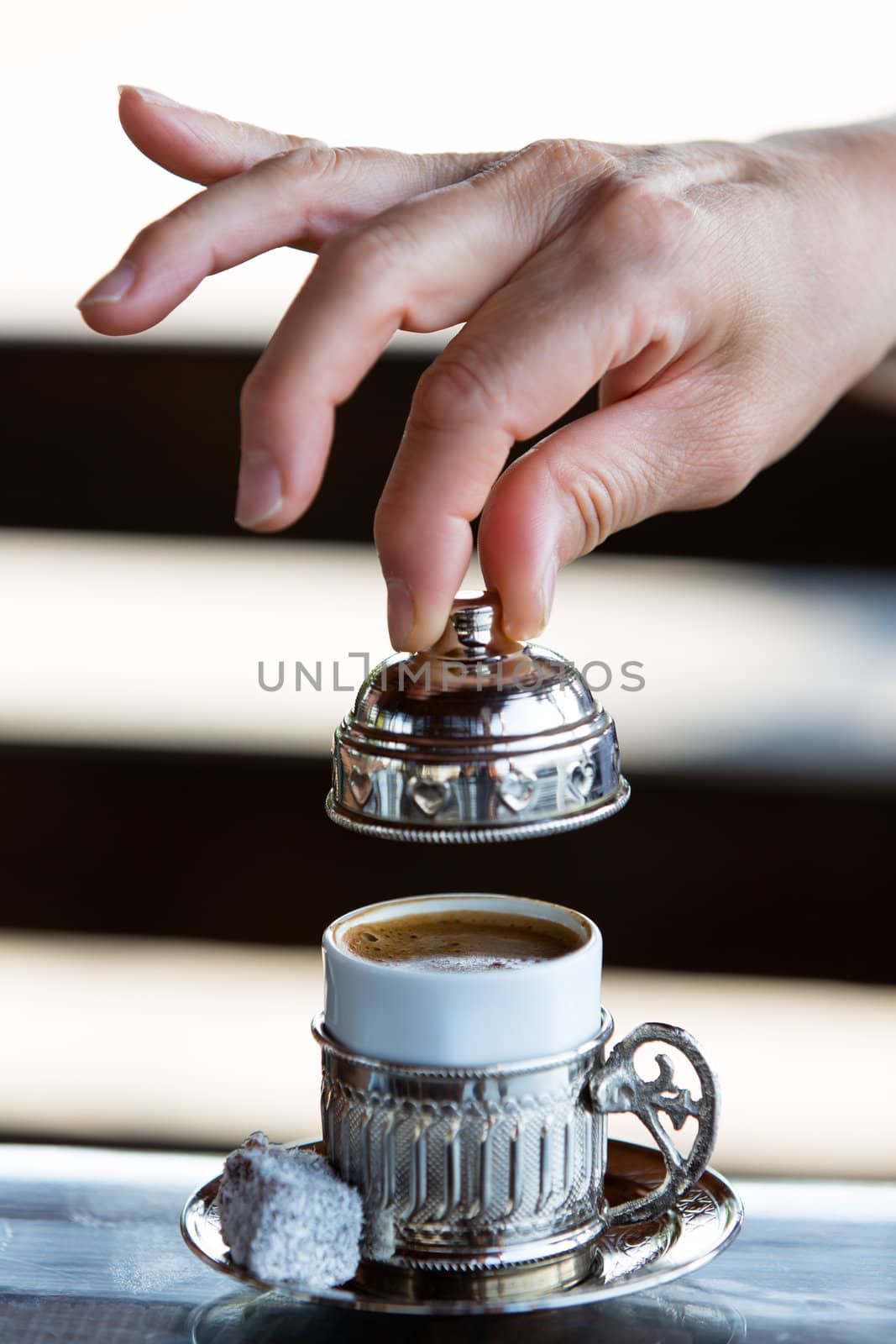 Turkish Coffee served in silver housing with a Turkish delight and ready to take a sip. Clean hands elegantly removing the cap.