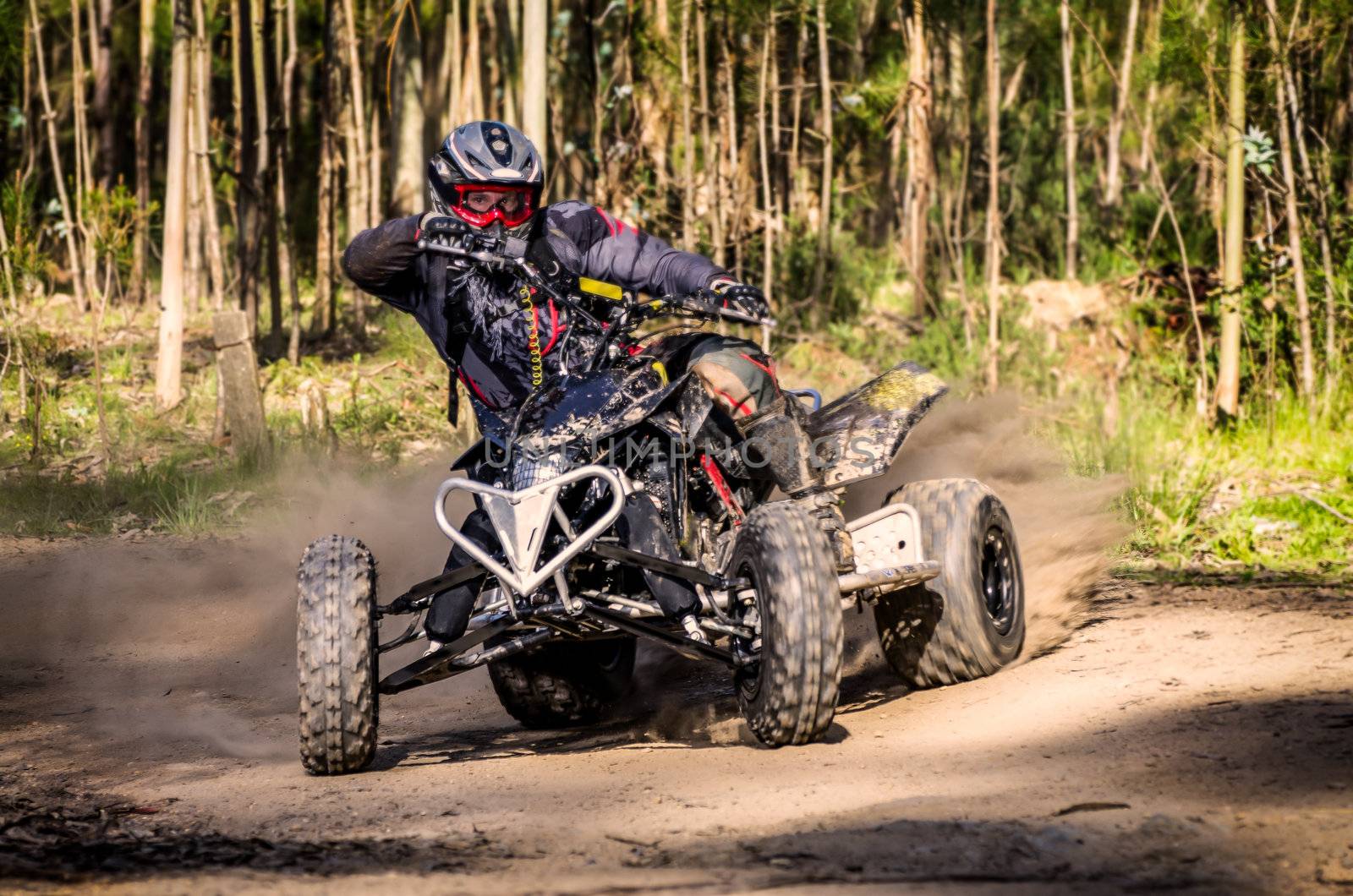 ATV racer takes a turn during a race on a dusty terrain.