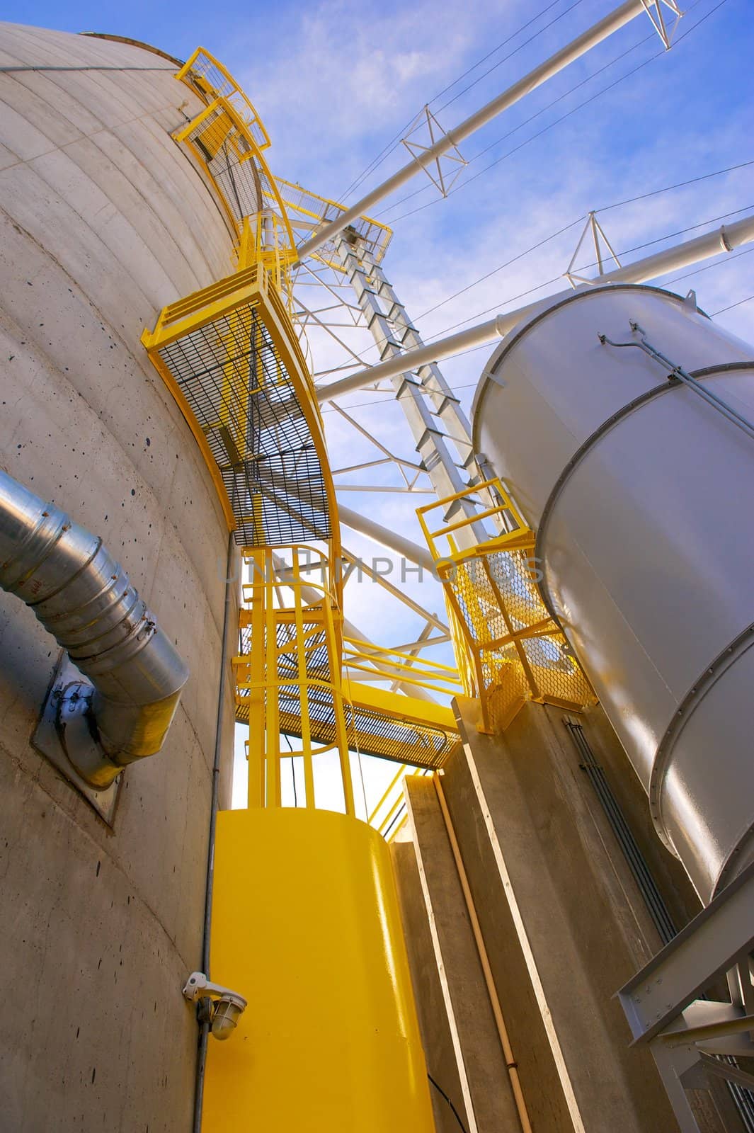 Vertical shot of towering grain silos made of concrete with metal conduits and yellow access areas at a food processing plant