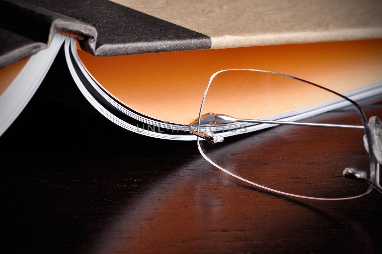 Eyeglasses next to an open book on top of a wood table