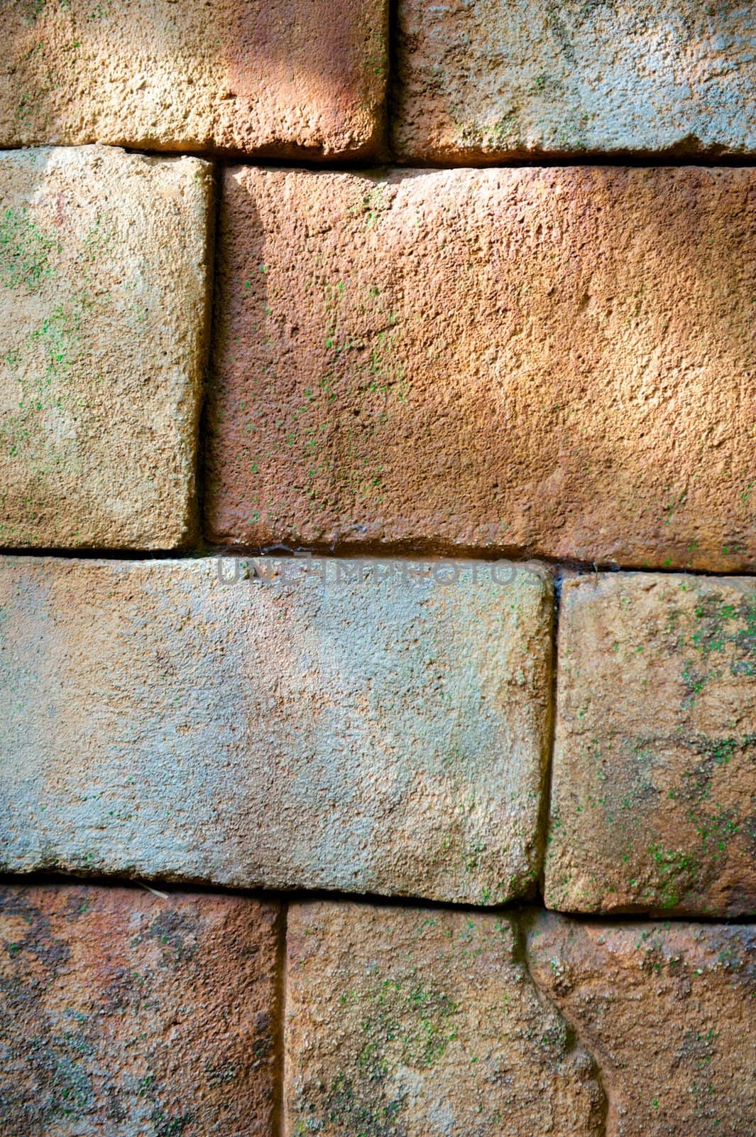 Vertical shot of a rough stone wall with green moss