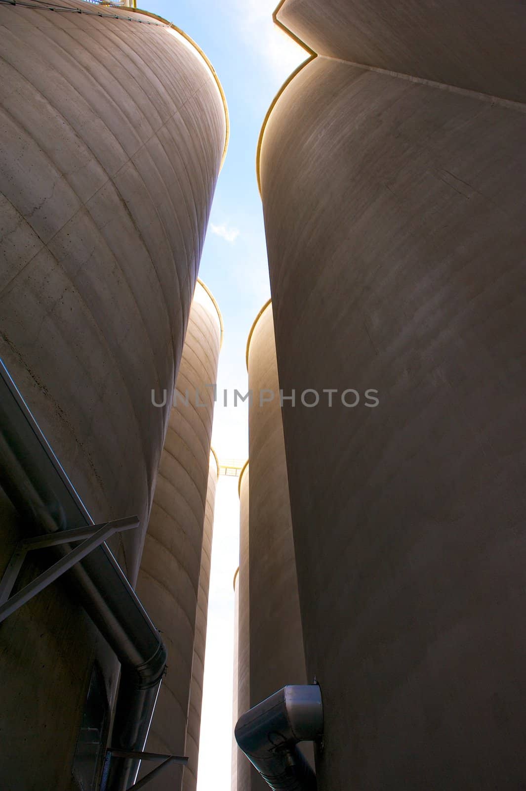 Vertical shot of two rows of towering grain silos made of concrete with metal conduits at a food processing plant
