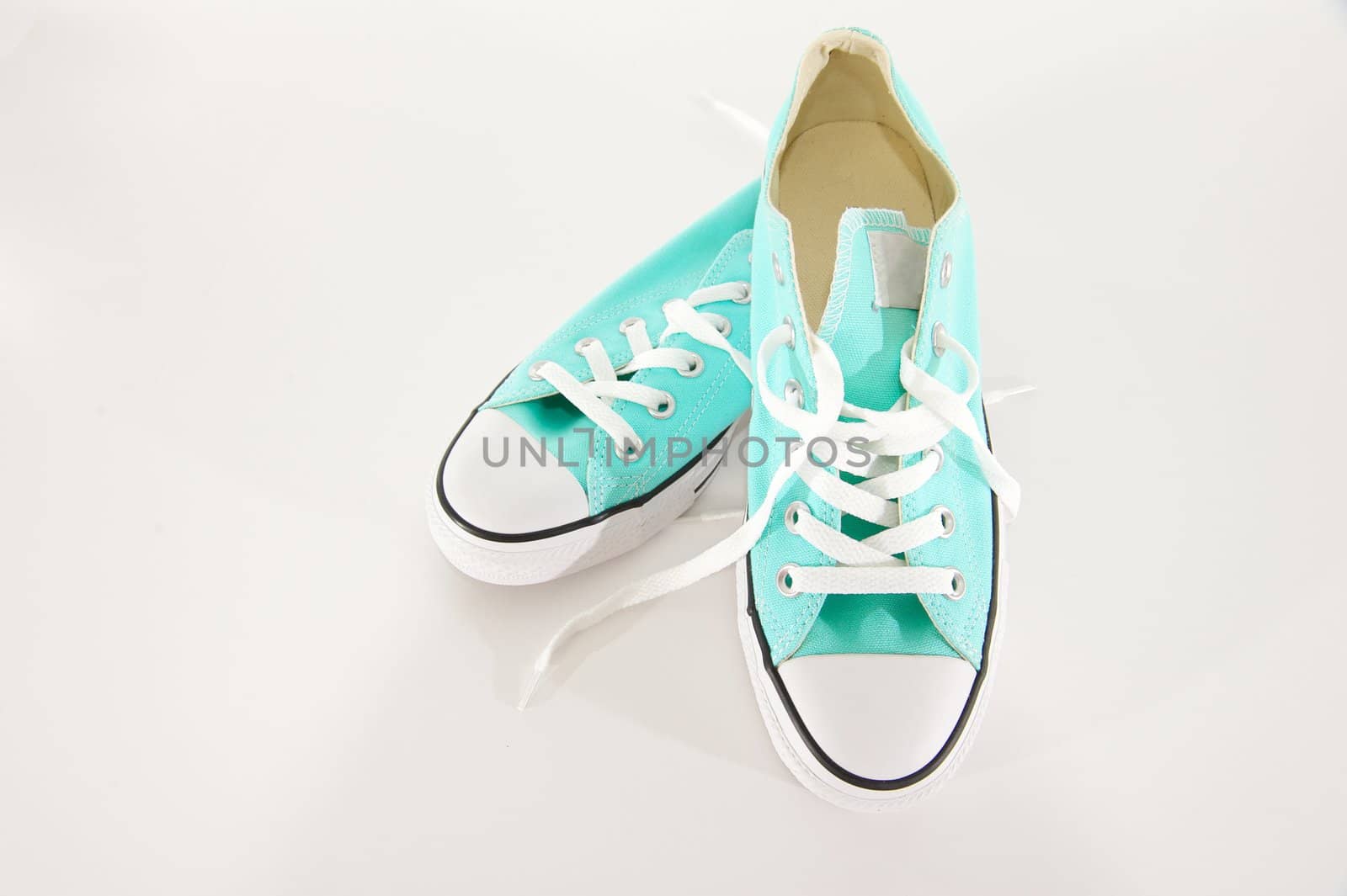 Pair of turquoise and white sneakers with laces on a blank background