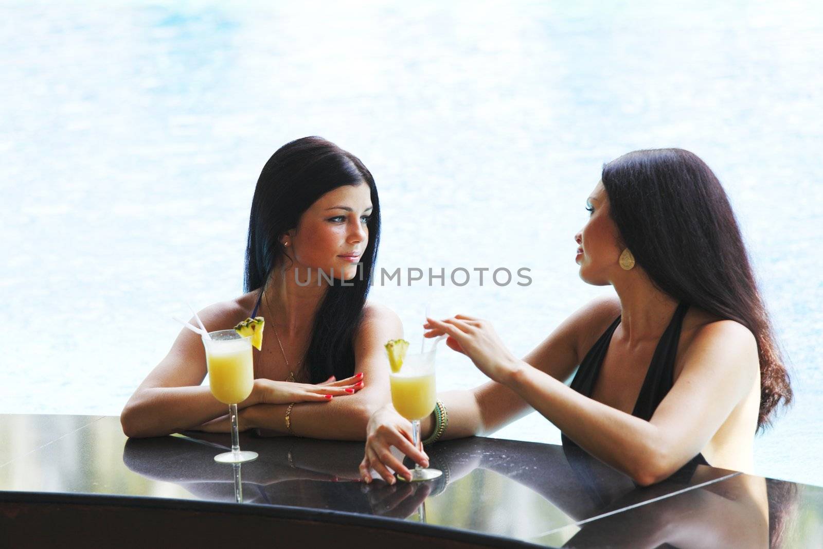 Two beautiful women relaxing in swimming pool with cocktails