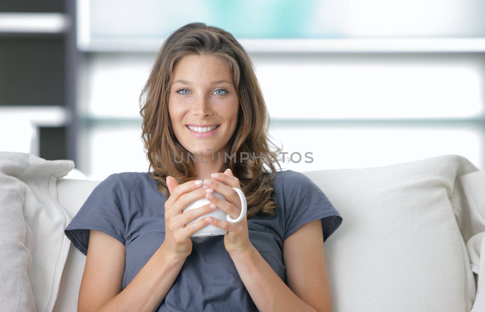 Portrait of a cute young lady sitting on sofa with a cup of coffee