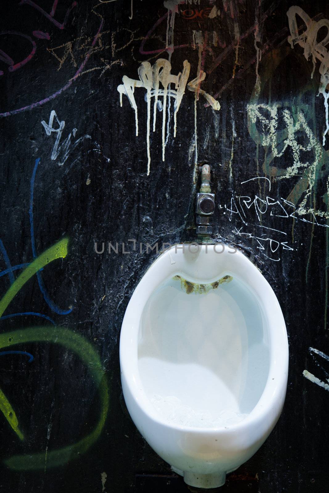 Old grungy white urinal against graffitis wall