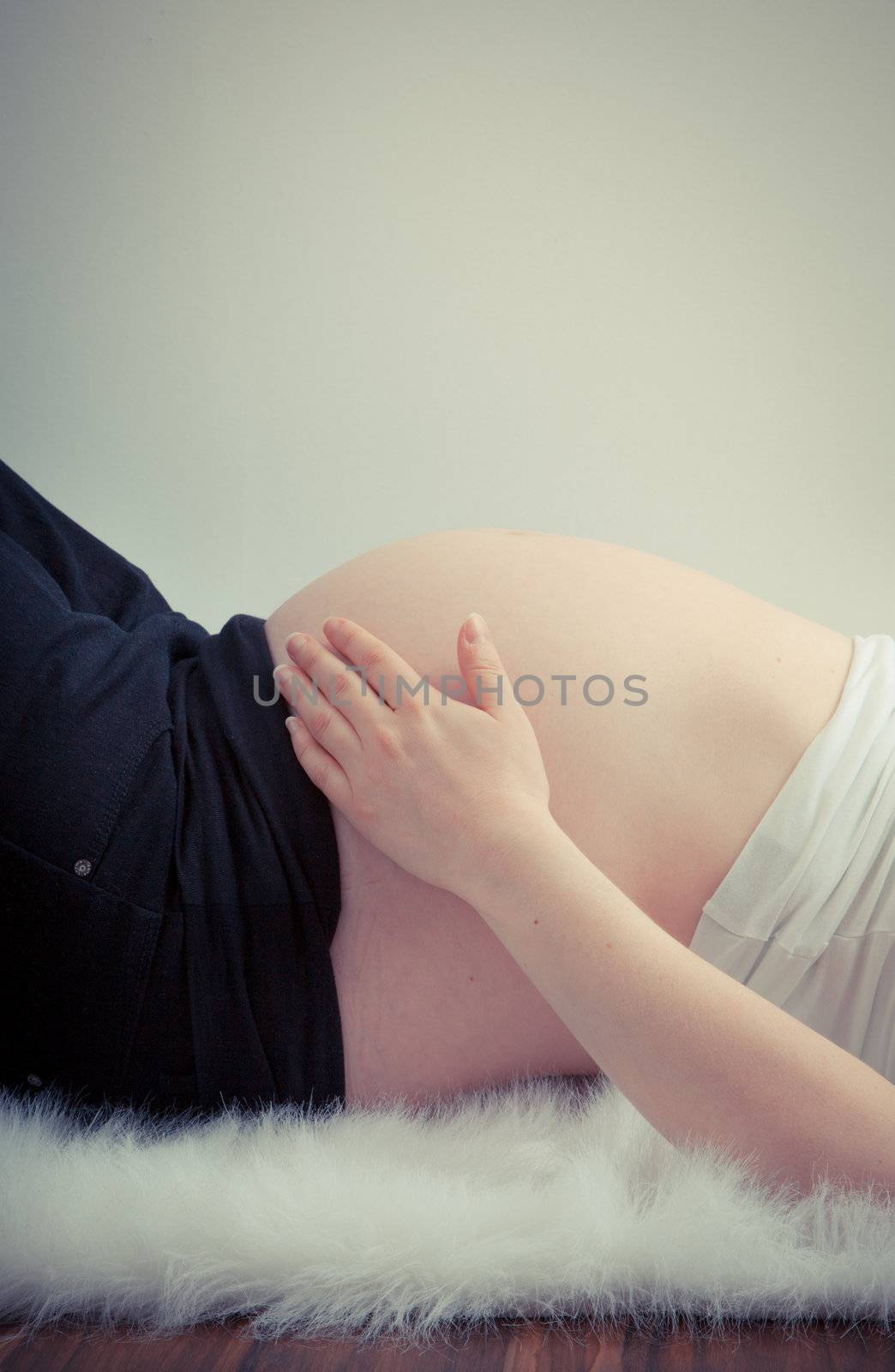 Hand holding pregnant belly lying on white fur  by Izaphoto