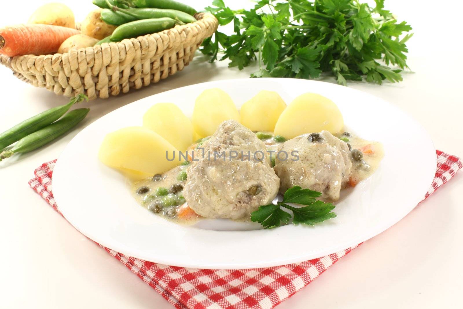 cooked meatballs in a white sauce with capers, vegetables and potatoes on a light background