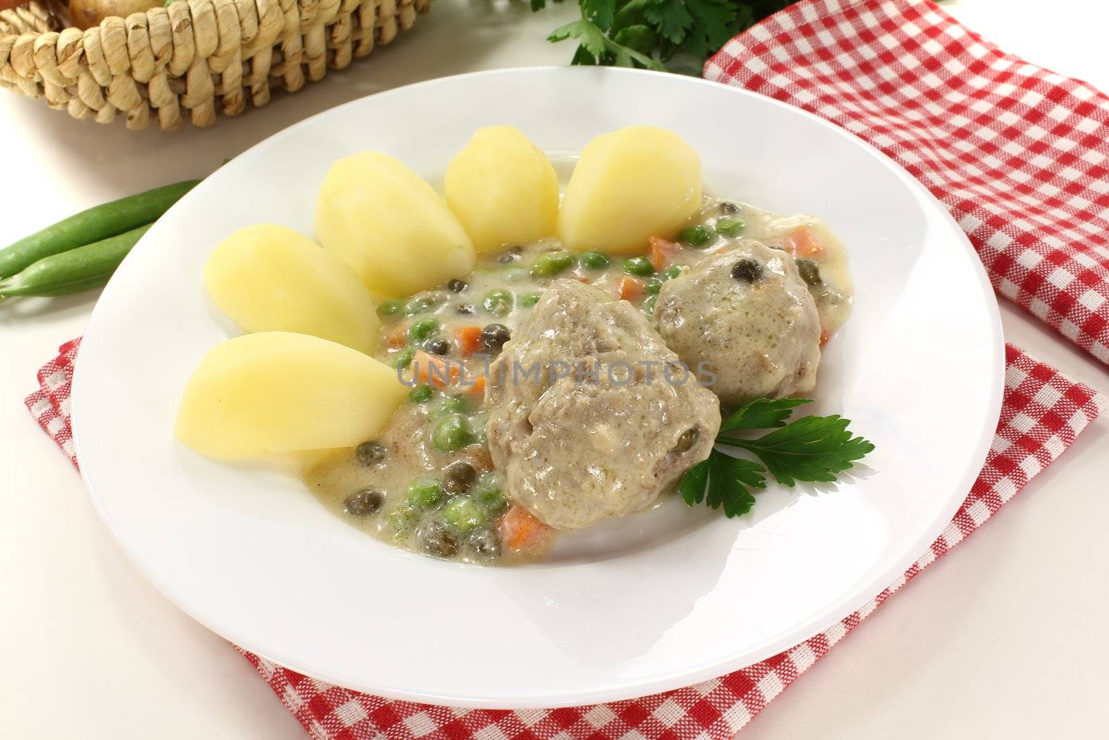 delicious cooked meatballs in a white sauce with capers, potatoes and parsley on a light background