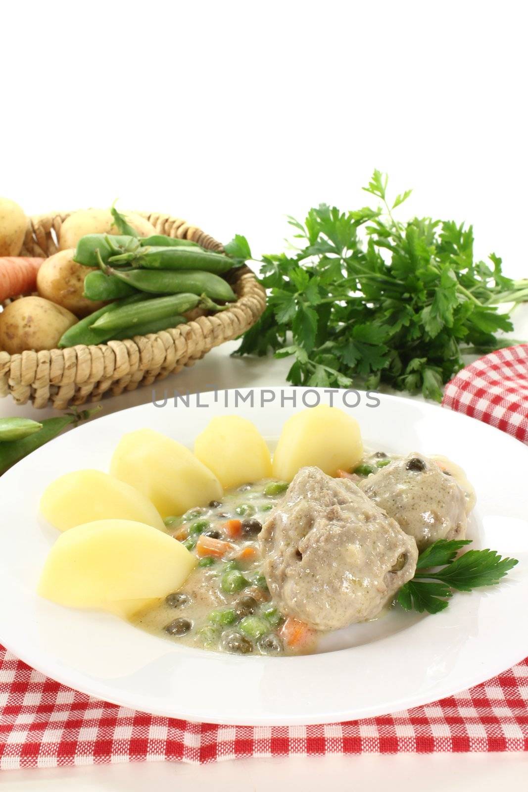 fresh cooked meatballs in a white sauce with capers, carrots and potatoes on a light background