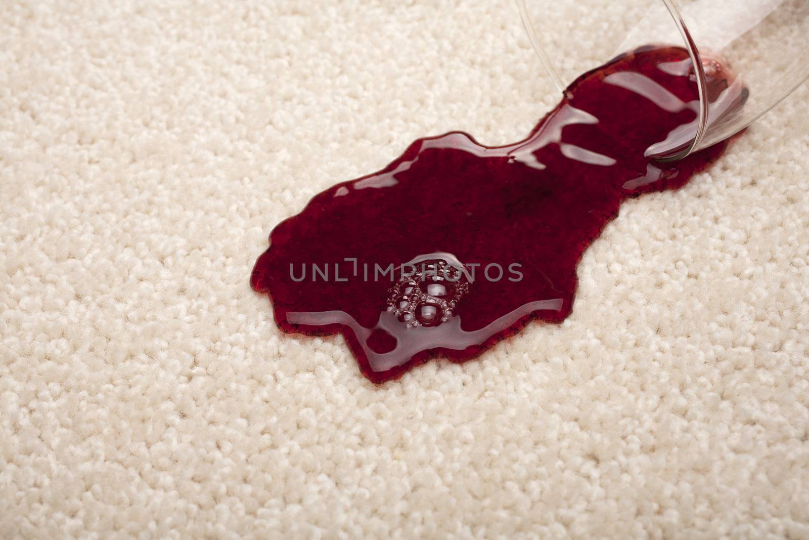 Red wine spilling from a glass onto a light coloured carpet.