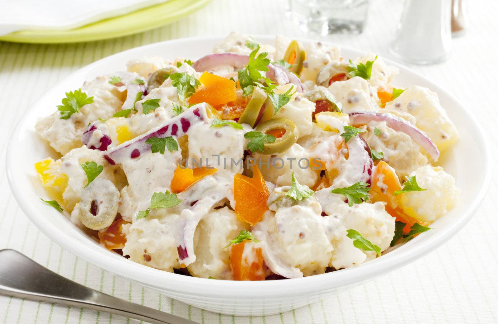 A bowl of potato salad with creamy mustard dressing. Salad also includes orange and yellow peppers, red onions and stuffed olives.