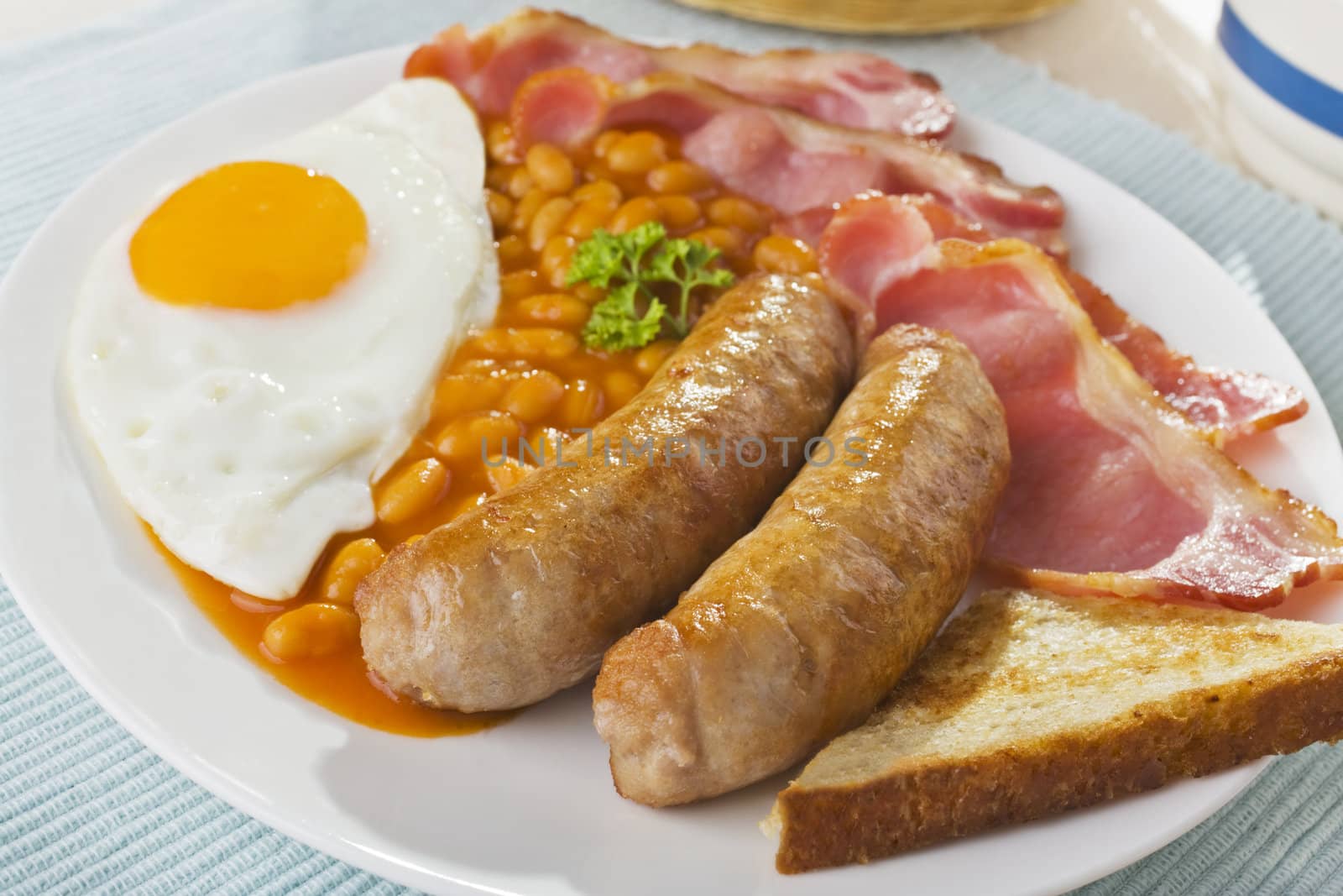 English breakfast of bacon, fried egg, baked beans sausages and fried bread..