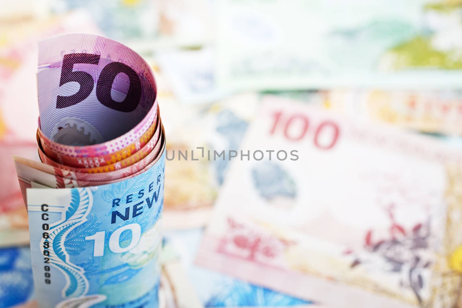 Rolled up New Zealand banknotes standing on an out of focus background of notes.