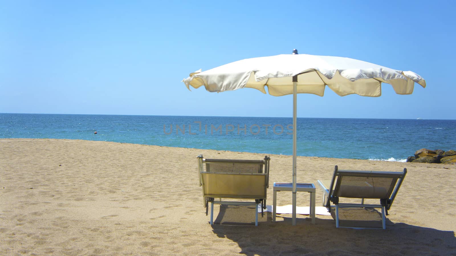 Two chairs a table and a white umbrella on the beach.