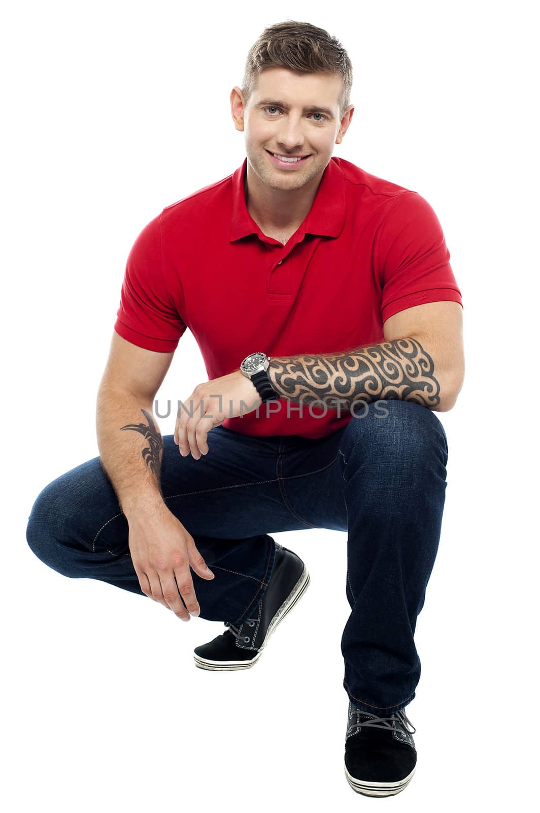 Young man sitting in squatting position. Wild tattoos on hands