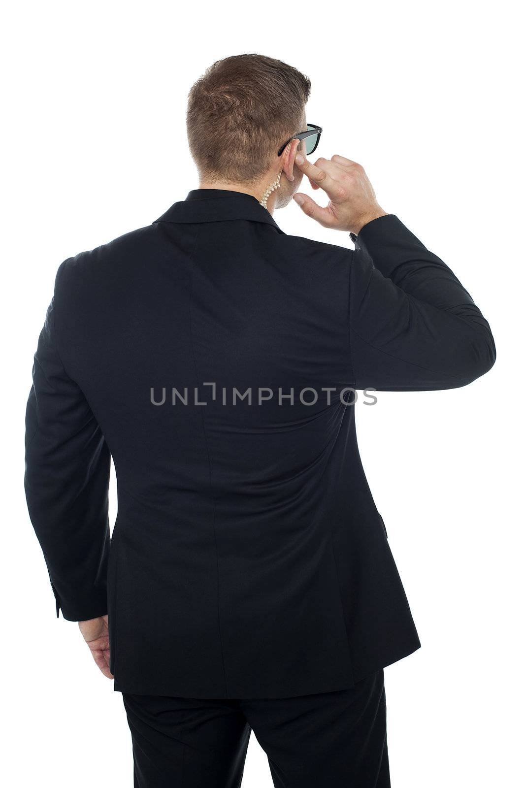 Bodyguard listening to vital information carefully while holding his earpiece. Back pose
