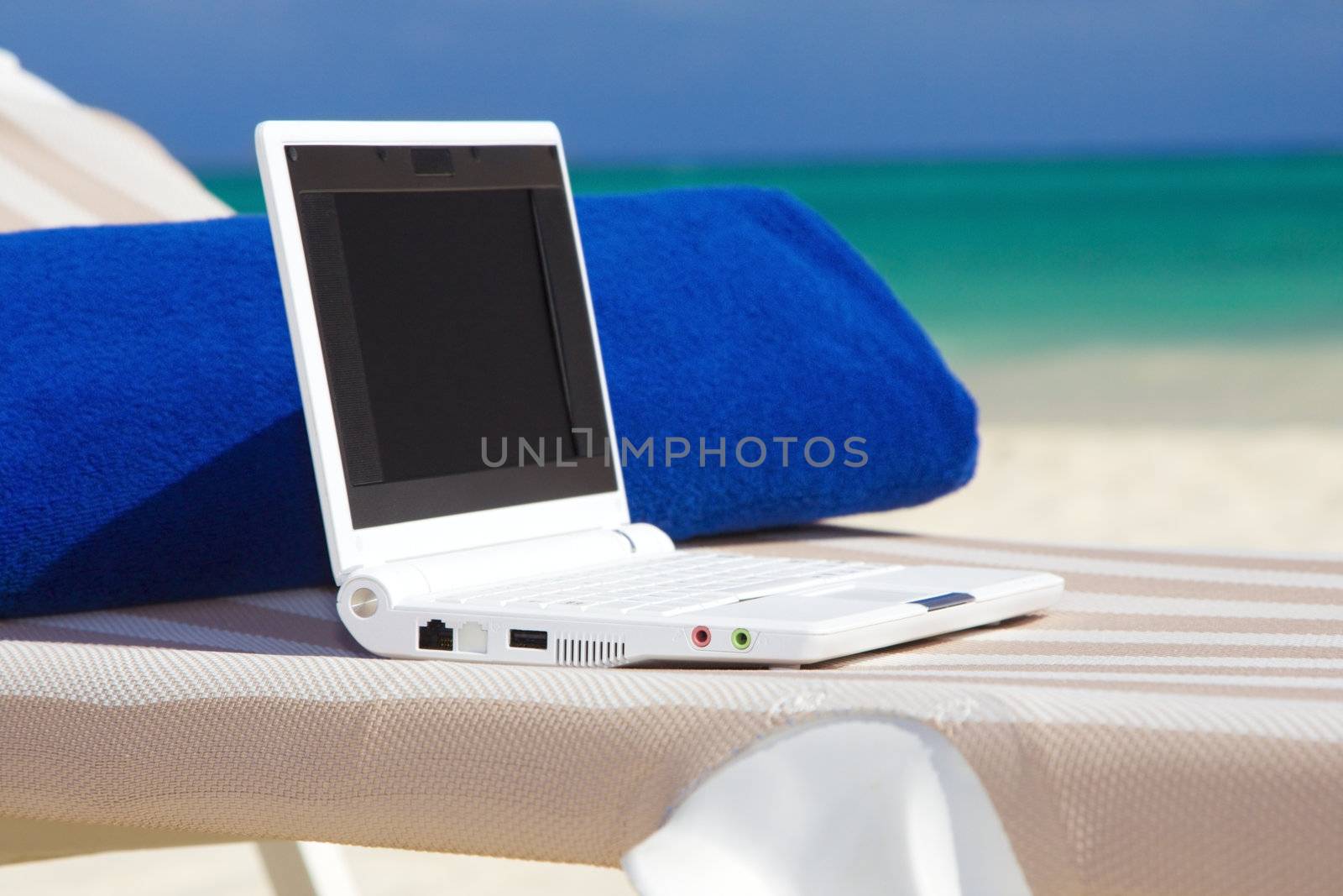 laptop and towel on the beach chaise longue by dolgachov