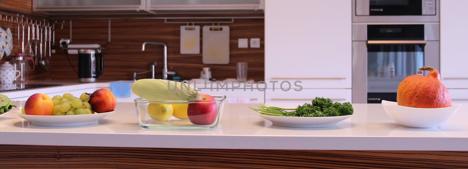  
Well designed modern kitchen with a big variation of ripe fruit and vegetables on the table
