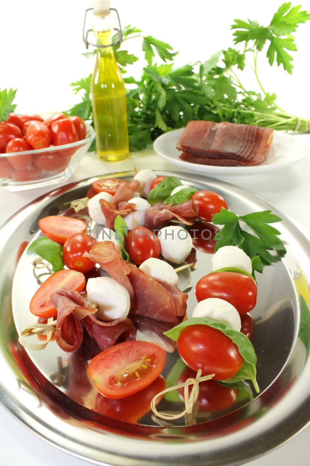 Tomato, mozzarella and ham skewers with basil on a light background