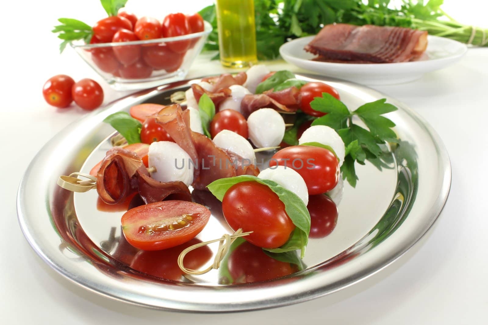 delicious Tomato, mozzarella and ham skewers with basil on a bright background