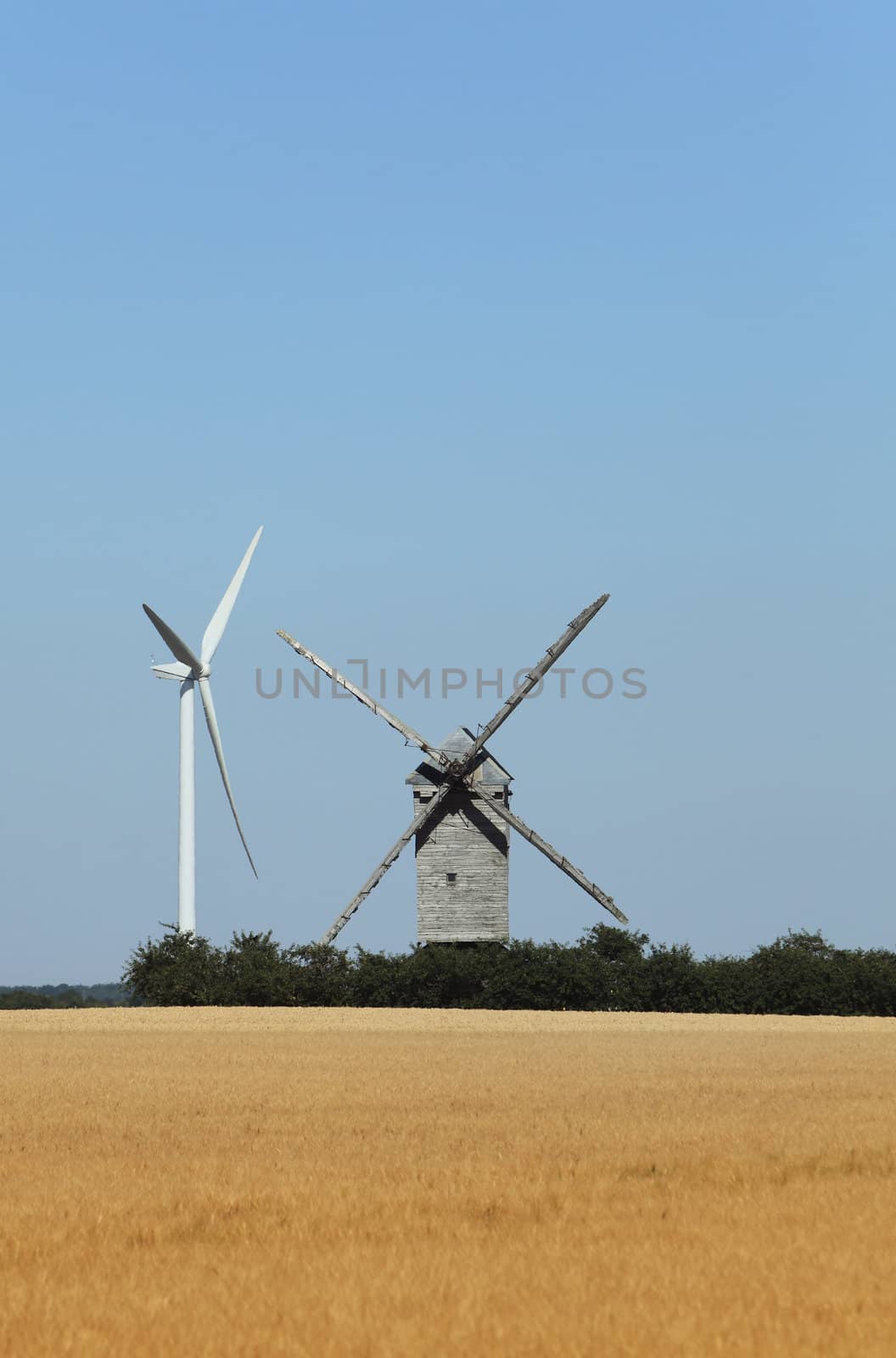 Image of a traditional windmill close to a modern eolian turbine in a cereal field. 