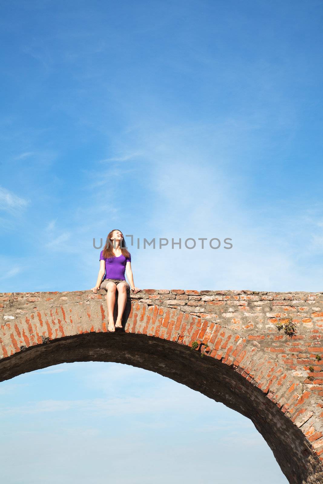 Young woman sitting outdoors against blue sky