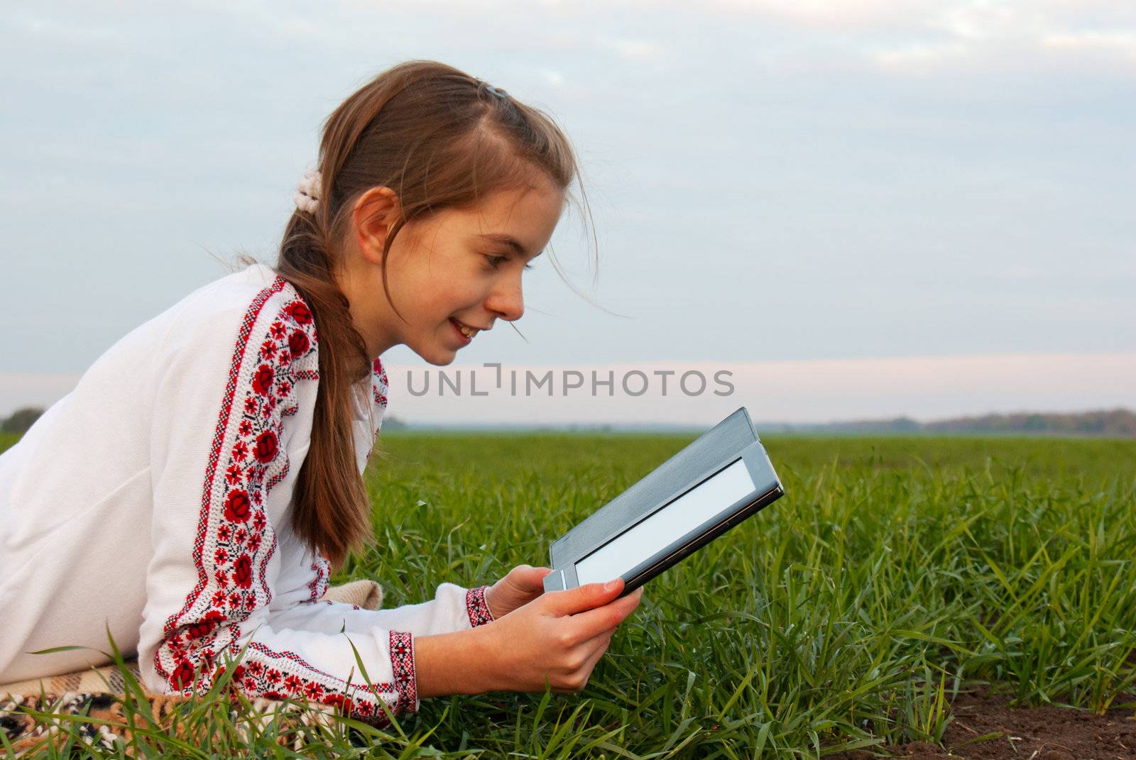 Teen girl with electronic book laying on grass at field