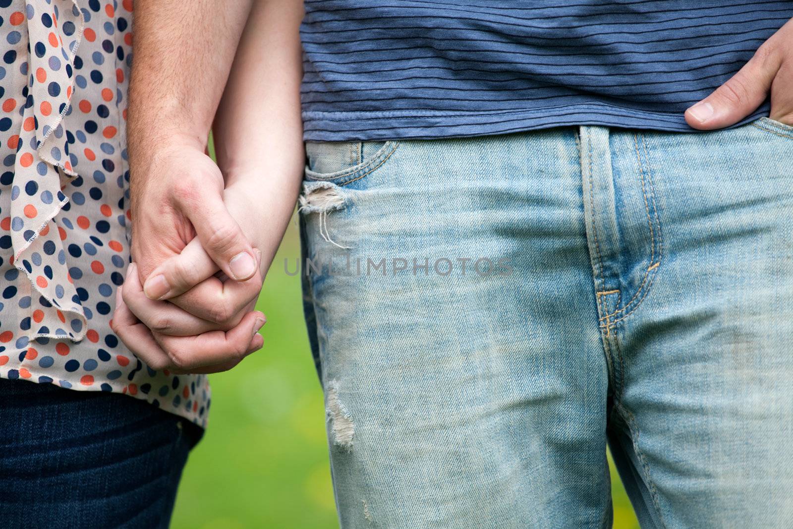 Close up of a young happy couple holding hands together at waist height.