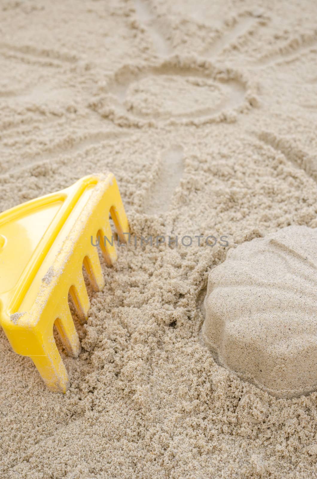 Closeup of sun drawn in sand with shell made of sand and toy rakes next to it.