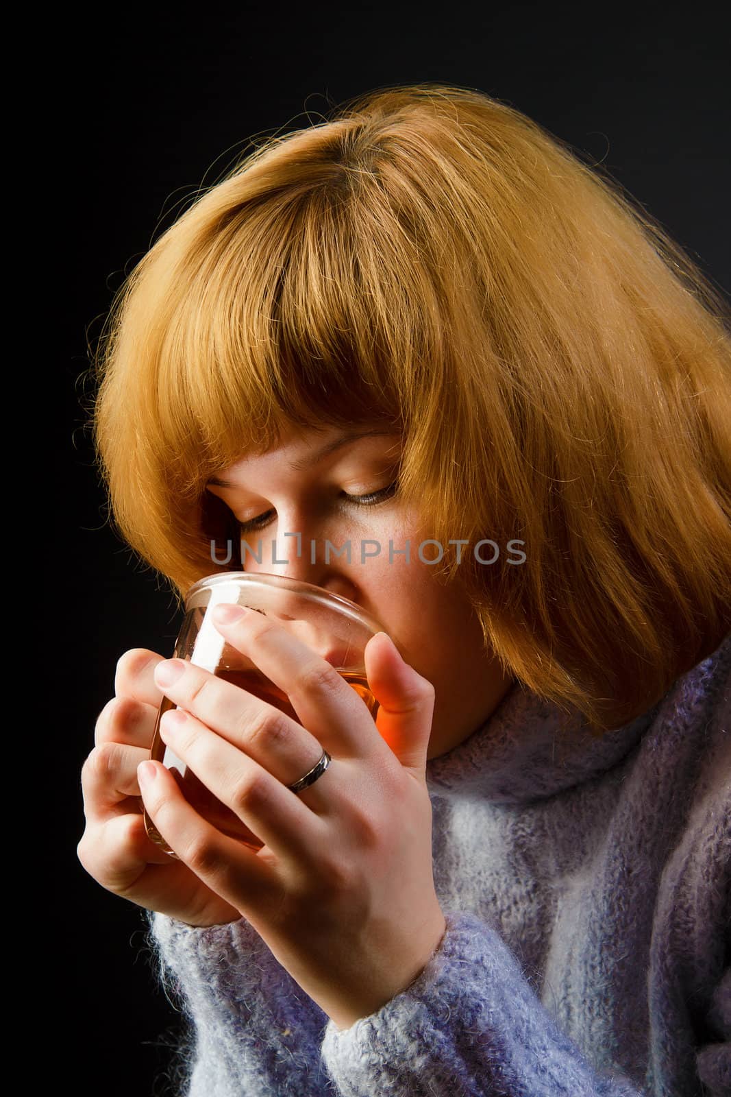girl in a sweater on a black background drinking tea from a transparent cup. portrait