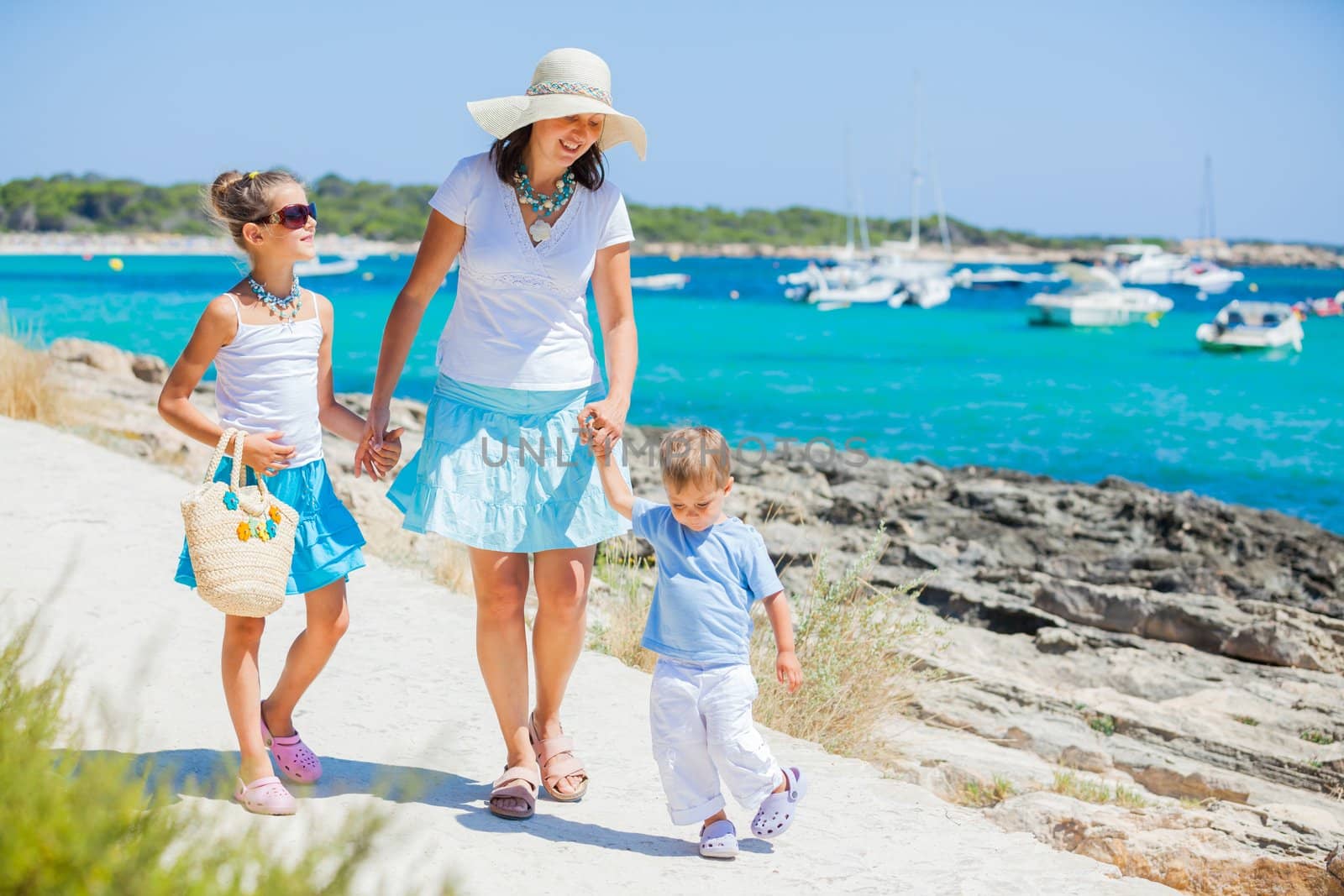 Young beautiful family of three walking along tropical beach