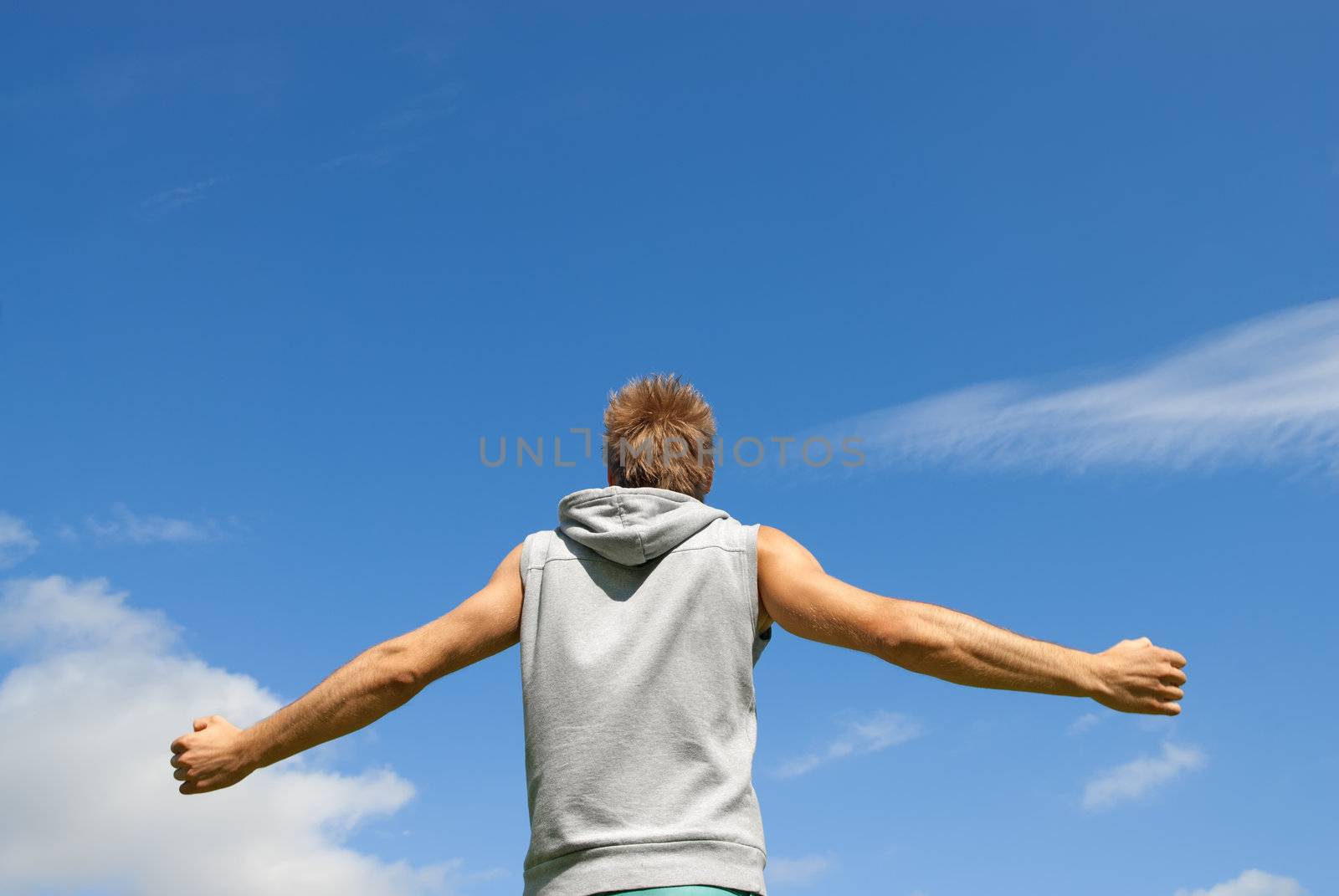 Guy in sports clothing, with his arms spread, looking at blue sky.