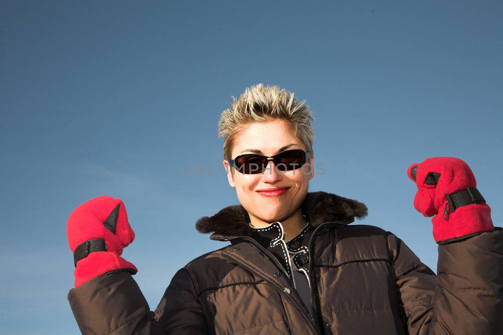 woman outdoor in winter shot against a blue sky in the sun playing with red gloves