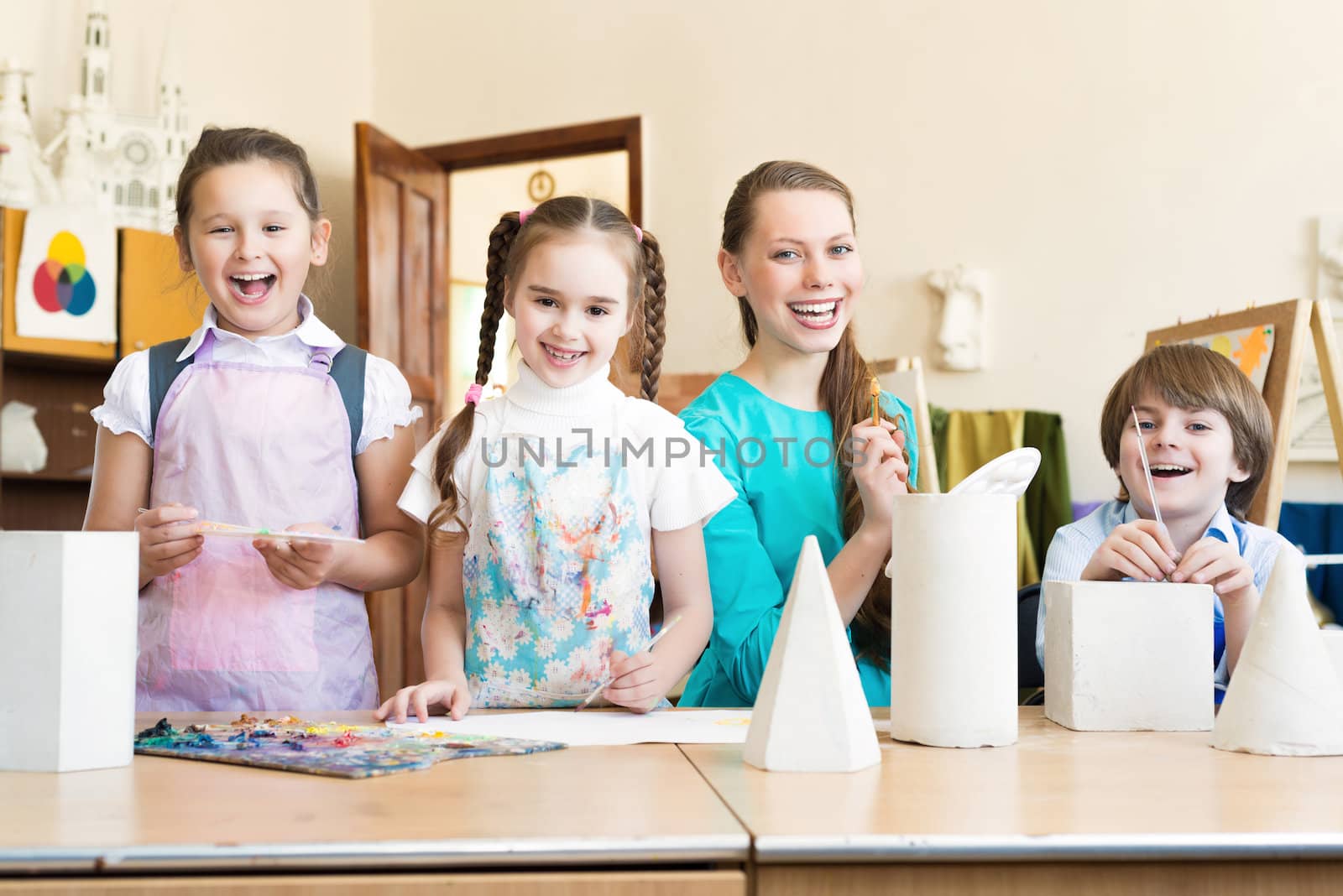 children with the teacher standing at the table, smiling and looking into the cam