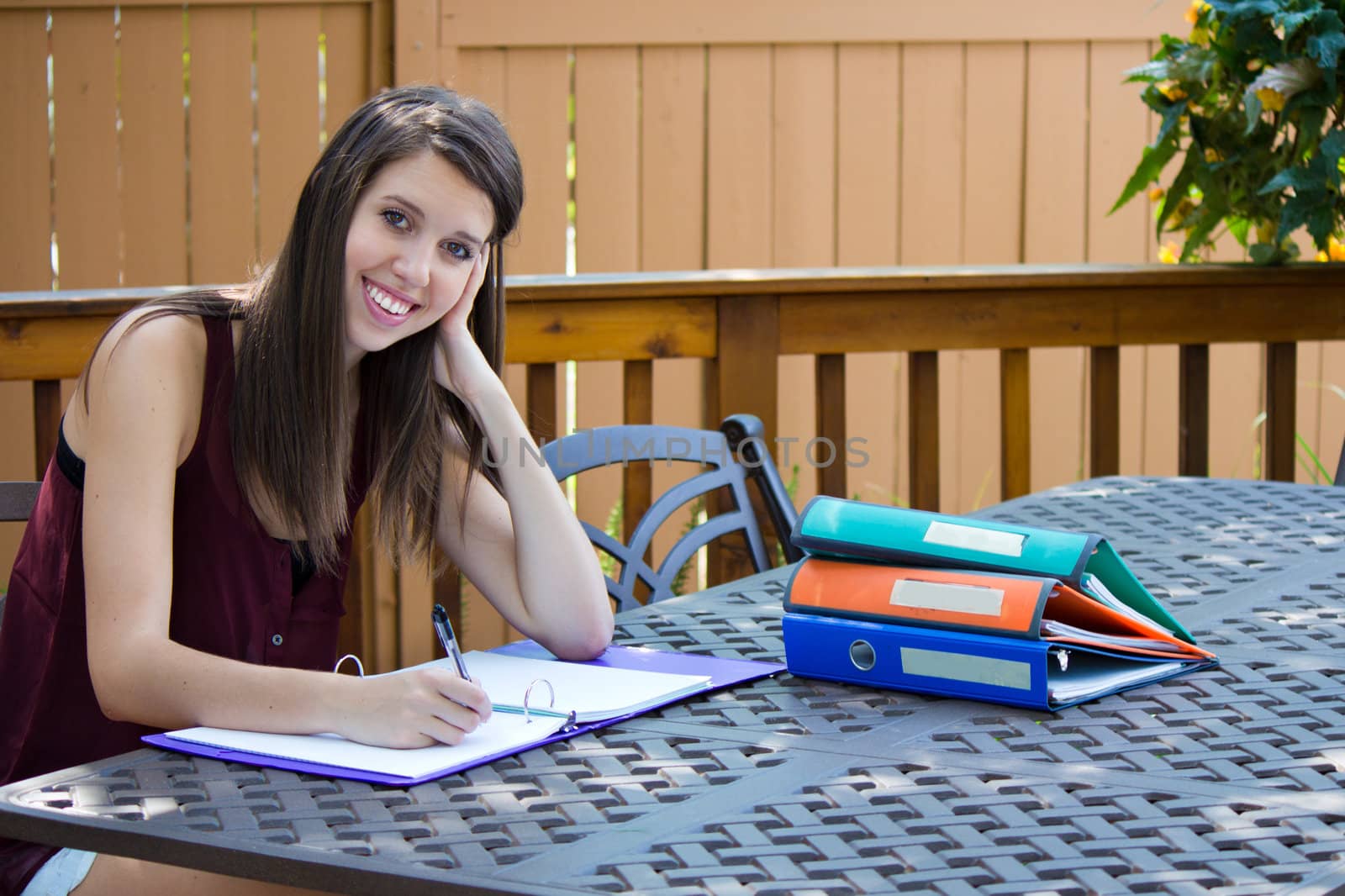 A pretty girl doing homework on a patio outside.