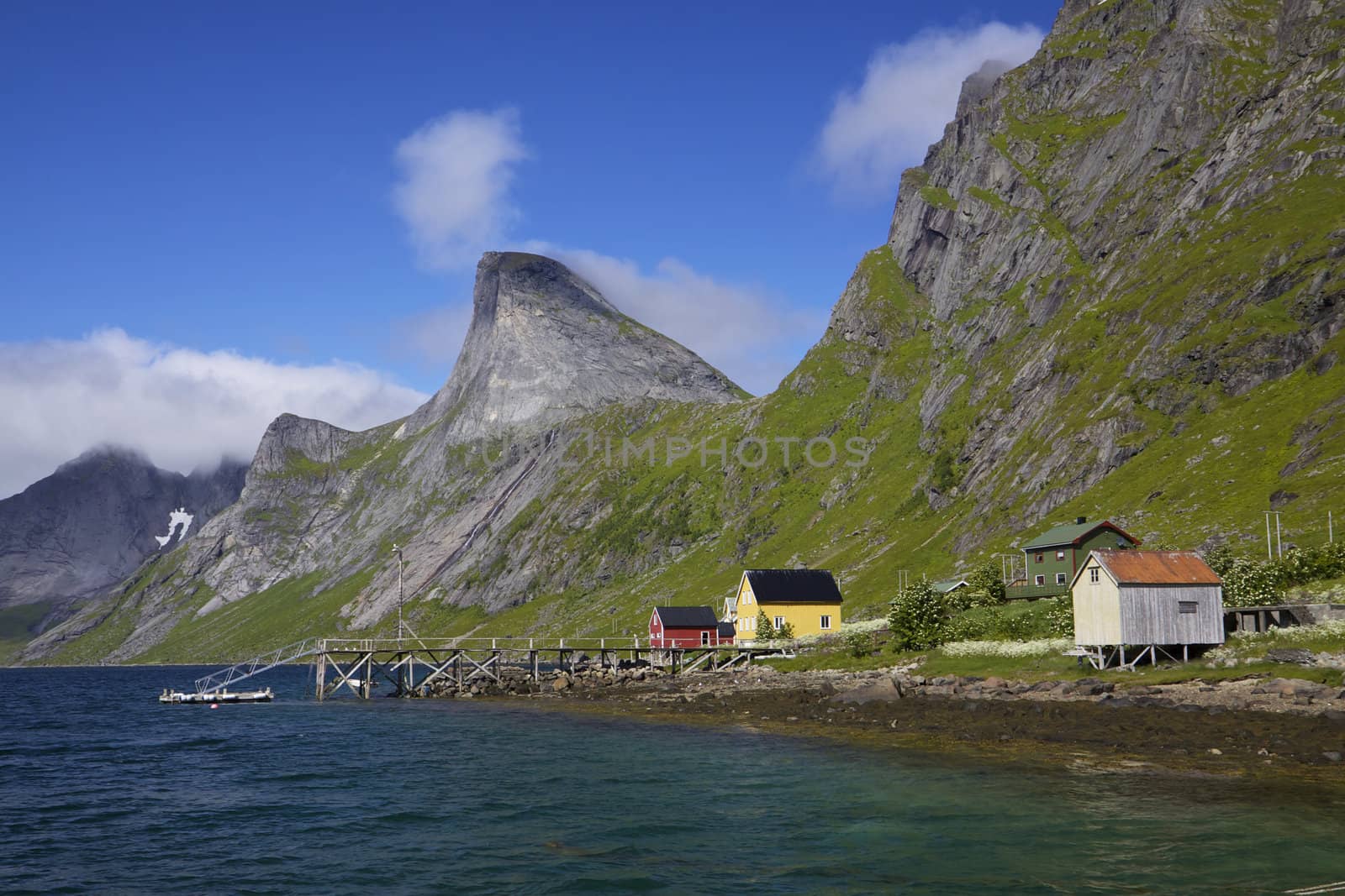 Small norwegian village by fjord near Reine on Lofoten islands, with dramatic mountain peaks towering above