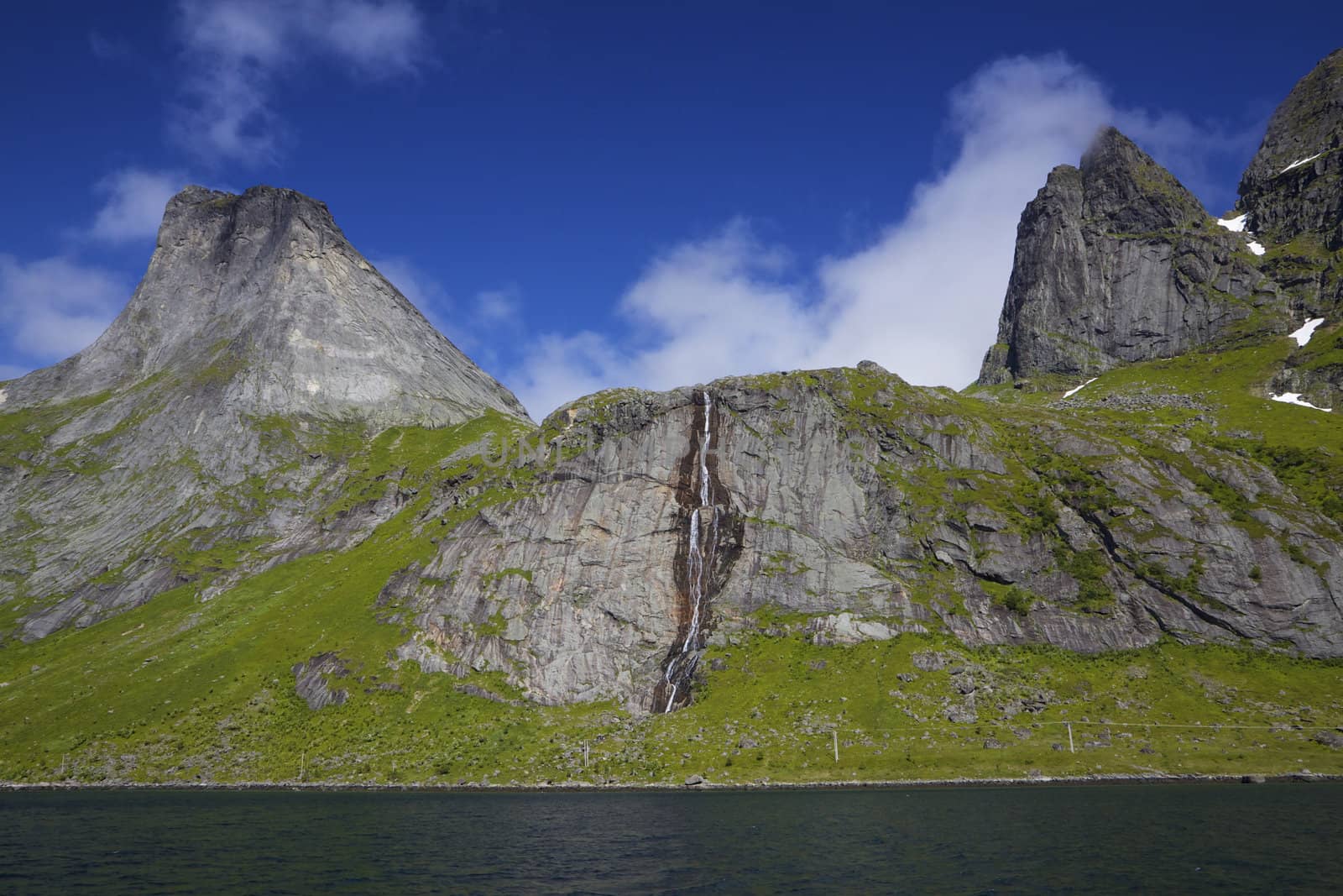 Towering peaks of mountains with waterfall around fjord on Lofoten islands in Norway