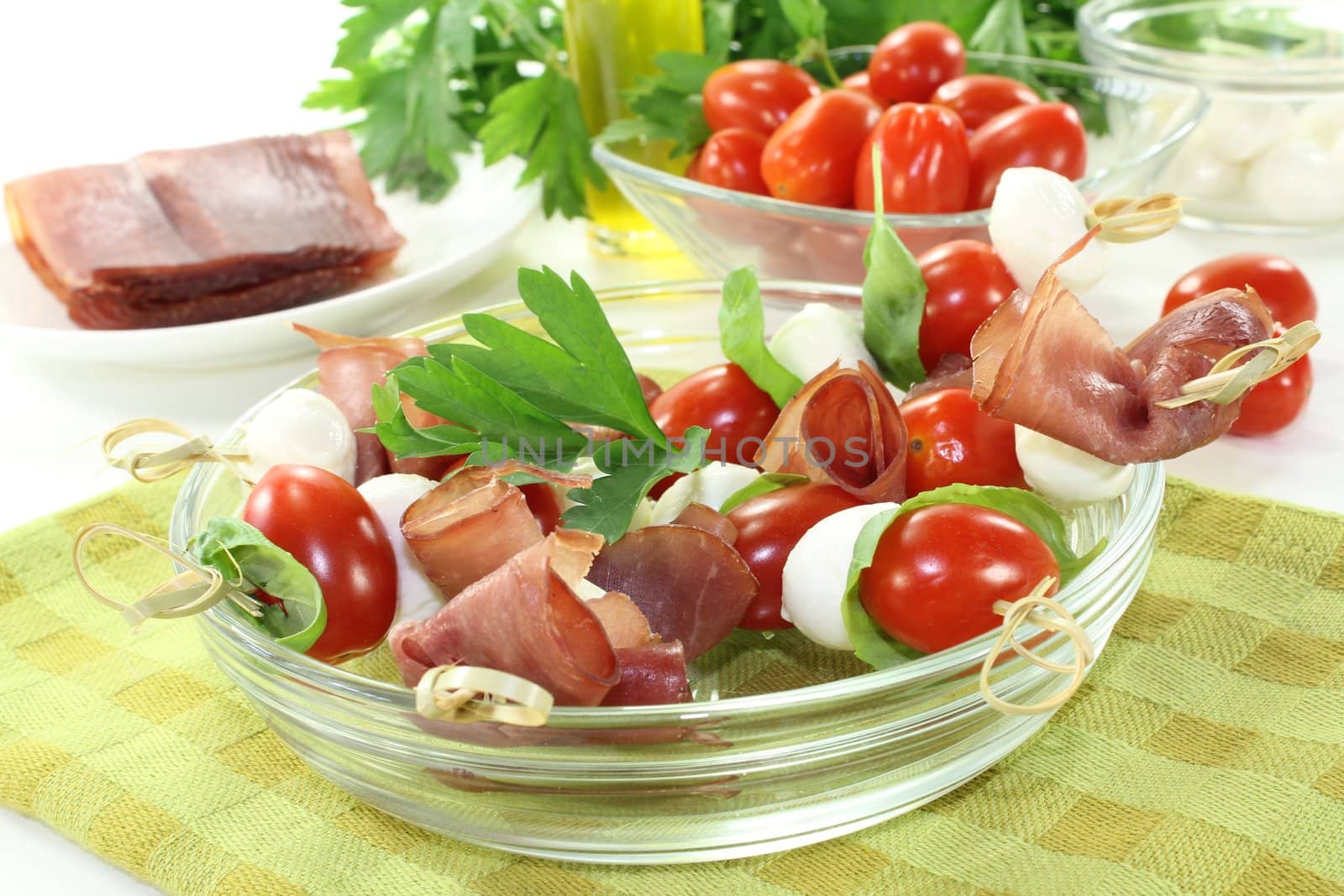 fresh Tomato, mozzarella and ham skewers with basil on a napkin before light background
