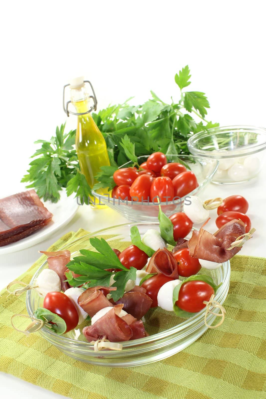 Tomato, mozzarella and ham skewers with basil on a green checkered napkin before light background