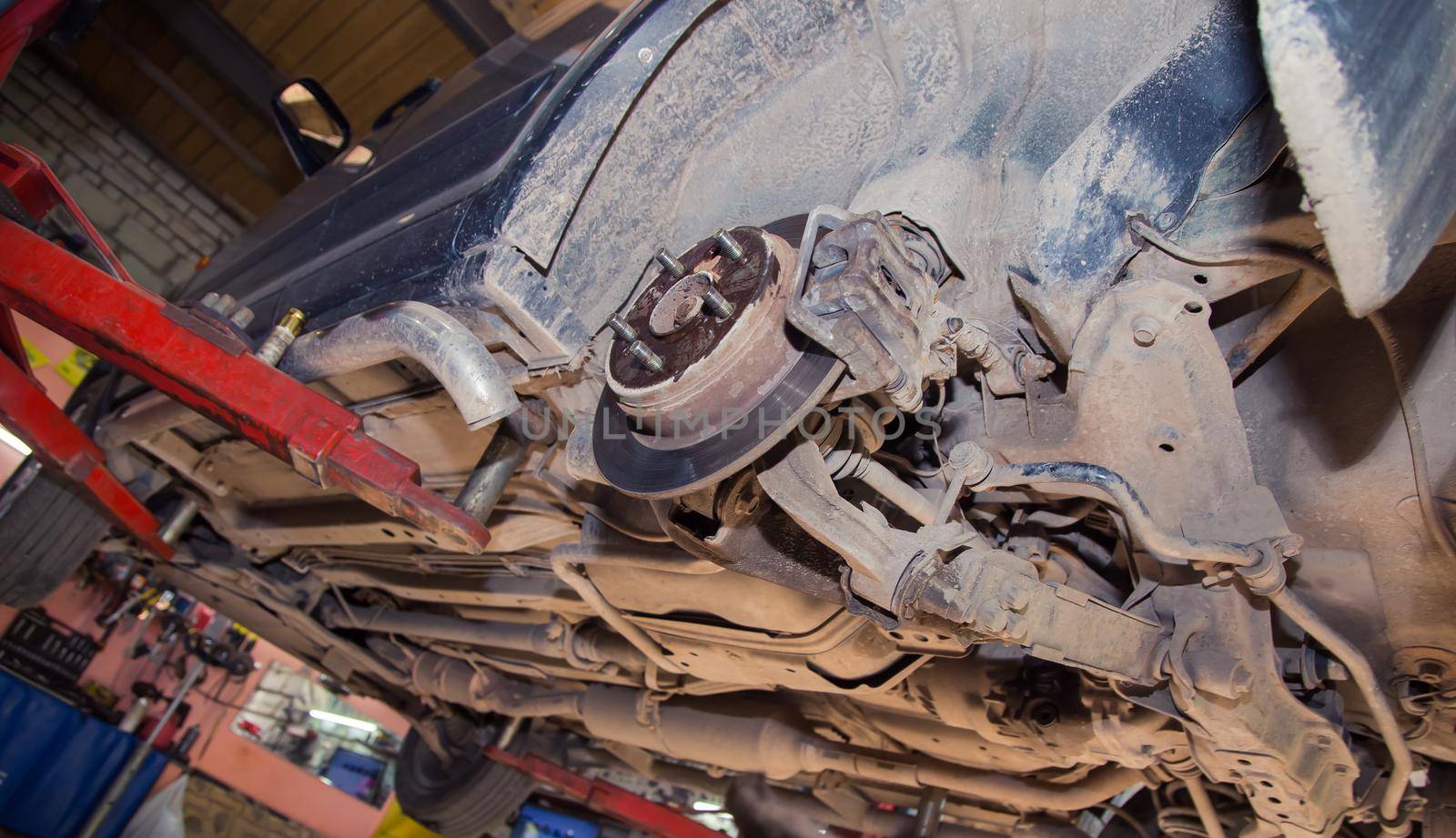 Bottom view of the undercarriage of an old car on a lift. In the garage, a man changes parts on a vehicle. Small business concept, car repair and maintenance service. UHD 4K.