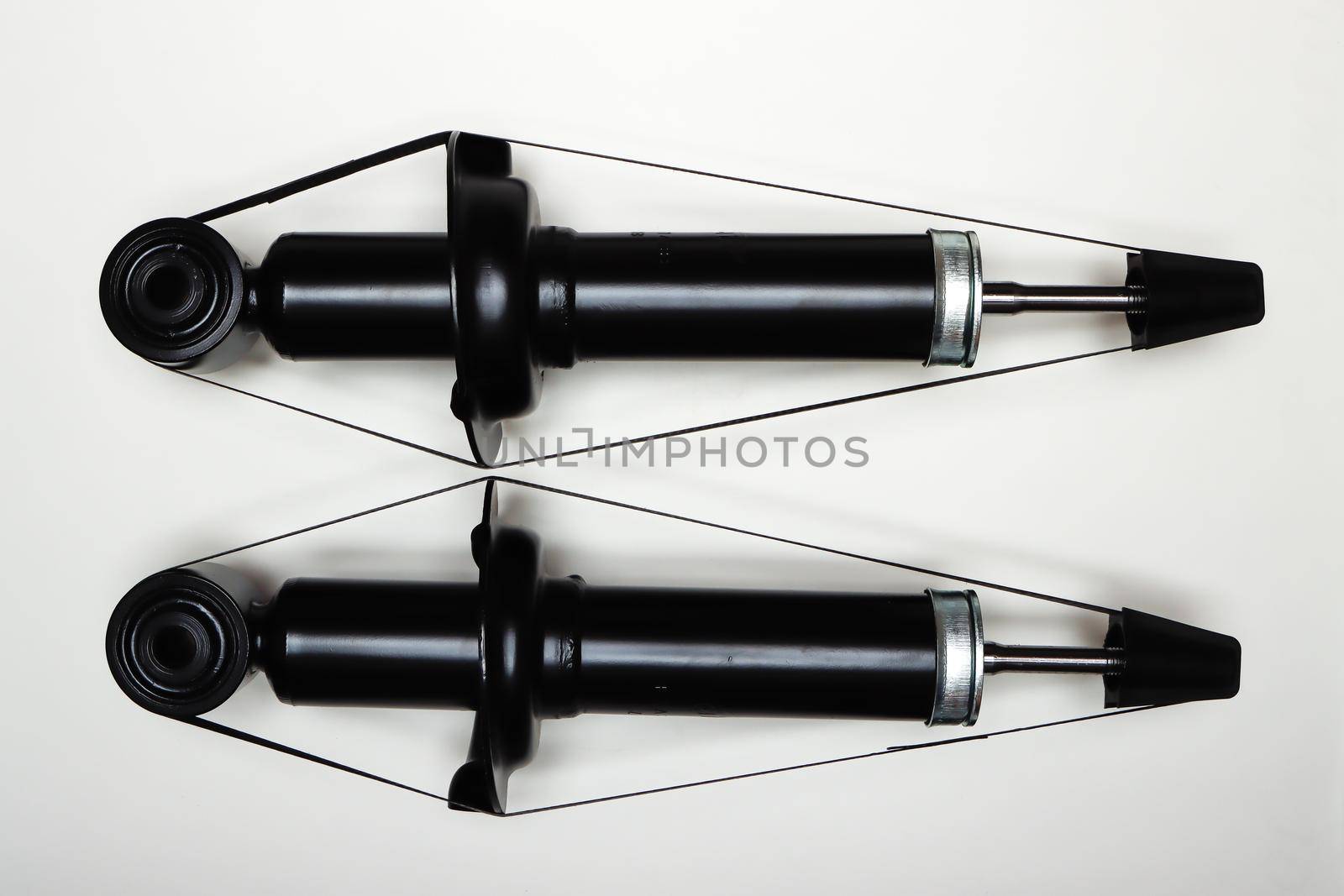 Two new shock absorbers for the car on a flat surface. A set of spare parts for the repair of the chassis of the vehicle. Details on white background, copy space available. UHD 4K.