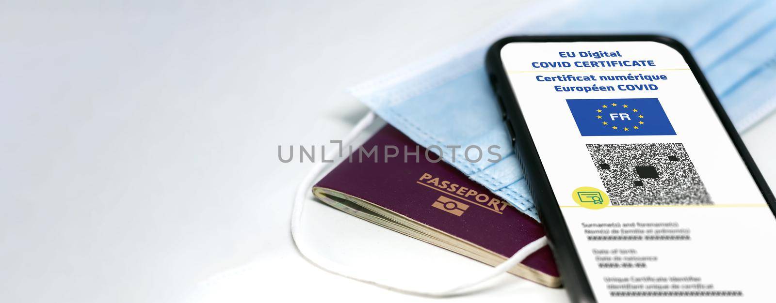 French EU Digital COVID Certificate with the QR code on the screen of a mobile phone over a surgical mask and a french passport by rarrarorro