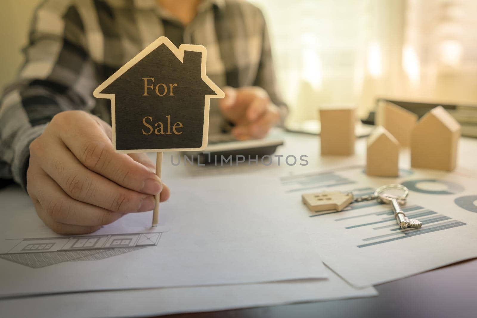 Real estate agents showing message For Sale on the sign of house shape on the table with a calculator, key, house design document, home wooden model. by pravinrus